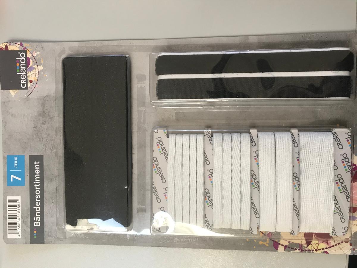 Bänder-Sortiment, Foto siehe Anlage,
- Warenzusammenstellung, bestehend aus vier Elastikbändern, einem Klettband und zwei
  Bügelsaumbändern,
- gemeinsam in einer Blisterpackung mit einer bedruckten Pappunterlage aufgemacht und zur
  Befriedigung eines speziellen Bedarfs zusammengestellt,
- Elastikbänder:
-- als Meterware; laut Antrag mit einer Breite zwischen 6 mm und 25 mm und einer Länge zwischen 1 m
   und 3 m,
-- aus ca. 1 mm dicken, einfarbigen Gewirken aus laut Antrag 60 GHT bis 65 GHT Polyester
   (synthetische Chemiefasern) und 35 GHT bis 40 GHT Kautschukfäden,
-- keine Elastomergarne enthaltend,
-- ohne Flor- oder Schlingenoberfläche,
- Klettband:
-- bestehend aus einem Hakenband (Samtgewebe mit Flor) der Position 5806 und einem Flauschband
   (Schlingengewebe mit Flor) der Position 5806; beide aus laut Antrag Polyamid,
--- jeweils:
---- mit einer Breite von ca. 16 mm und einer Länge von laut Antrag 1 m,
---- mit unechten Webkanten an den Längsseiten,
---- auf der Rückseite mit einer mit dem bloßen Auge wahrnehmbaren Klebeschicht überzogen und mit
     einem Abdeckpapier versehen,
---- von Hand bei einer Temperatur zwischen 15 und 30 °C auf einen Dorn von 7 mm Durchmesser
     aufrollbar, ohne rissig zu werden.
- Bügelsaumbänder:
-- als Meterware; mit einer Breite von ca. 25 mm bzw. 30 mm und einer Länge von laut Antrag 2 m,
-- aus zwei mit ihrer ganzen Fläche aufeinanderliegenden und so miteinander durch Nähen verbundenen
   Lagen:
--- mit einer Ober- und Unterlage:
---- aus einem Gewebe aus synthetischen Chemiefasern (laut Antrag Poyester), 
---- mit Schmelzklebepunkten bedruckt,
---- in Leinwandbindung,
- die sog. Elastikbänder bestimmen insbesondere im Hinblick auf den Umfang (Menge) den Charakter
  der Warenzusammenstellung.

"Gewirke mit einer Breite von weniger als 30 cm und mit einem Anteil an Kautschukfäden von mehr als
 5 GHT, andere als solche der Position 6001"