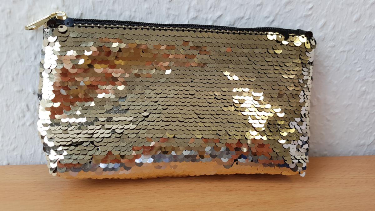 Ähnliches Behältnis, sog. Schmucktäschchen, Foto siehe Anlage,
- mit zwei verschiedenen Außenseiten:
- - an einer Seite aus einem mit Pailletten bestickten Stickgrund aus Gewebe aus Spinnstoffen
    (Applikationsstickerei der Position 5810), wobei die Pailletten aus Kunststoff (= Außenseite) den
    Stickgrund bedecken und den mit bloßem Auge wahrnehmbaren Stoff an der Oberfläche bilden,
- - an der anderen Seite mit einer Außenseite aus Kunststofffolie,
- - die Fläche der beiden die Außenseite bildenden Stoffe ist gleich; die Außenseite aus Pailletten
    aus Kunststoff ist insbesondere nach dem Erscheinungsbild (Schauseite) charakterbestimmend,
- mit einem entlang des oberen Rands verlaufenden Reißverschluss,
- gefüttert; ohne weitere Innenausstattung,
- in den Abmessungen: ca. 16,5 cm (Breite) x 10 cm (Höhe) x 4 cm (Tiefe).

"Ähnliches Behältnis, anderes als in den Unterpositionen 4202 1110 bis 4202 3900 genannte, mit 
 Außenseite aus anderen Stoffen als in den Unterpositionen 4202 9110 bis 4202 9298 genannte"
