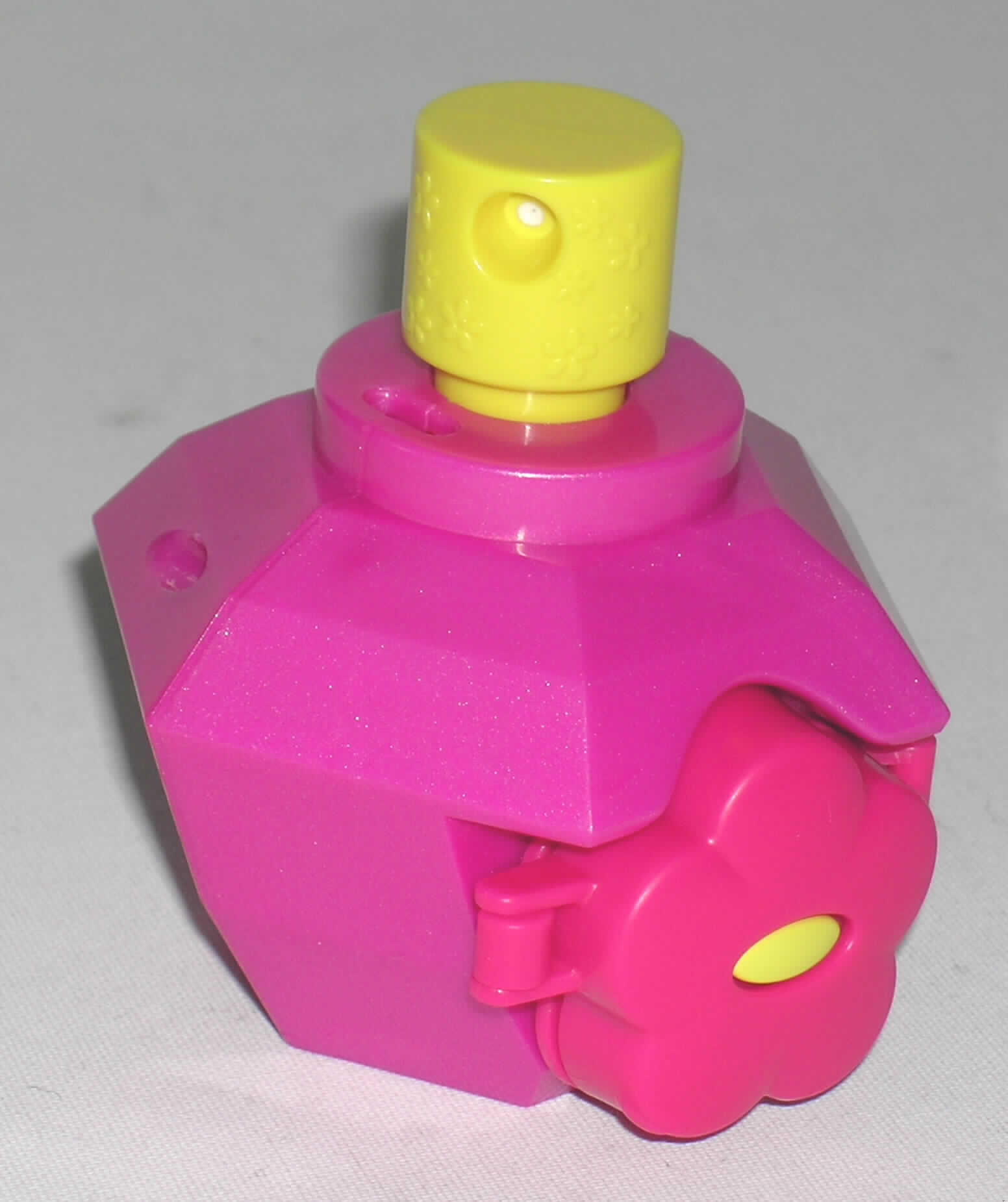 Zerstäuber zu Toilettenzwecken als zusammengesetzte Ware, sog. Mc Donald's - Spy 
Gear / Totally Spies 2007 "Secret Perfume Sprayer", bestehend aus einem magentafarbenen
Kunststoffbehälter zur Aufnahme von Flüssigkeiten in Form eines stilisierten, facettierten Diamanten mit einem Fassungsvermögen von 80 ml (Maße: H x B =  6,5 x 9 cm), mit einer
verschließbaren Einfüllöffnung am oberen Rand sowie einer aufgesteckten
Zerstäubervorrichtung aus Kunststoff, bestehend aus einem Sprühkopf mit Kolbenfeder und
einem Kolbenrohr mit Ansaugrohr zur Verwendung als Zerstäuber für bspw. Parfum.
Der Zerstäuber ist mit einer blütenförmigen, pinkfarbenen Haarspange (Durchmesser x Dicke = 4 x 1,5 cm) aus Kunststoff zusammengesetzt, die an einer speziellen Befestigungsvorrichtung am Flakongehäuse befestigt ist.
Der Zerstäuber ist charakterbestimmend hinsichtlich Größe und Erscheinungsbild und zusammen mit der Haarspange in einem Kunststoffbeutel verpackt.

Abbildung im Internet.