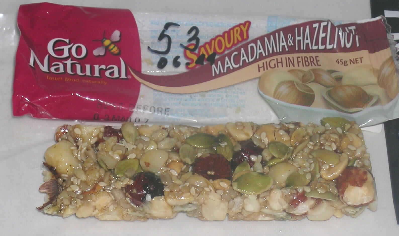 Antragsangaben (als zutreffend unterstellt): Riegel 4516SMH Macadamia & Hazelnut. Zutaten: Nüsse (Erdnüsse, Macadamianüsse 17 %, Haselnüsse 11 %), Honig 13 %, Glucose, Sonnenblumenkerne, Kürbiskerne, Sesamsamen, gepuffter Reis, Chicoreeextrakt (Inulin), feste Milchbestandteile.

Beschaffenheit der vorgelegten Warenprobe: Riegel (ca. 13 x 4 x 1 cm) aus verschiedenen, teilweise zerkleinerten Schalenfrüchten und anderen Samen. Geschmack: nussig (geröstet) und süß. Aufmachung: die Ware ist in einer bedruckten, transparenten Folienverpackung aufgemacht. Warenaufschrift (auszugsweise): "Go Natural, Macadamia & Hazelnut, High in Fibre, 45 g net". 

Früchte, Nüsse und andere genießbare Pflanzenteile, in anderer Weise zubereitet oder haltbar gemacht, auch mit Zusatz von Zucker, anderweit weder genannt noch inbegriffen, Schalenfrüchte, Erdnüsse und andere Samen, auch miteinander vermischt, andere, einschließlich Mischungen, in unmittelbaren Umschließungen mit einem Gewicht des Inhalts von 1 kg oder weniger, andere als tropische Nüsse, geröstete Nüsse, andere als Mandeln oder Pistazien.