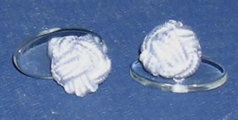 Manschettenknopf, bestehend aus einer länglich-ovalen, durchsichtigen Kunststoffplatte (Maße: 1,8 x 0,9 x 0,2 cm = L x B x D) in deren Mitte mittels einer Schlaufe eine knotenartige Kugel aus Spinnstoffen befestigt ist (Durchmesser: 1 cm). Die Spinnstoffkugel bestimmt hinsichtlich des Wertes den Charakter des Manschettenknopfes.

Abbildung im Internet unter: 
http://ec.europa.eu/taxation_customs/dds/ebticau_de.htm