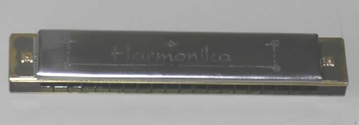 Blasinstrument in Form einer Mundharmonika, Länge 155 mm, bestehend aus einem Kanzellenkörper aus Kunststoff und Stahlblecheinfassungen, mit 20 Blasöffnungen (Kanzellen) für 20 Töne. Die Mundharmonika ist in einer bedruckten Pappschachtel verpackt.