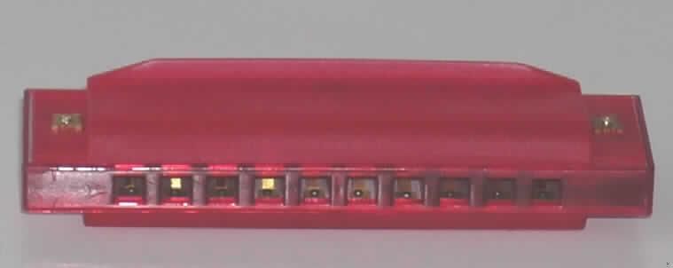 Blasinstrument in Form einer Mundharmonika, Länge 100 mm, bestehend aus einem Kanzellenkörper aus Kunststoff mit 10 Blasöffnungen (Kanzellen) für 10 Töne. Die Mundharmonika ist in einer Kunststoffschachtel verpackt.
