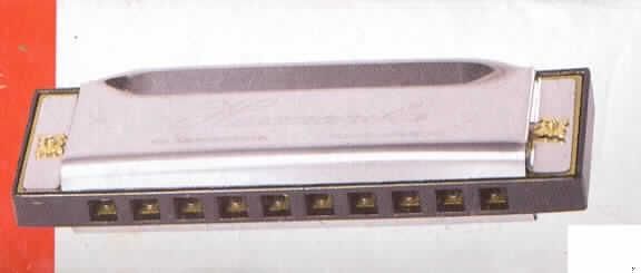 Blasinstrument in Form einer Mundharmonika, Länge 100 mm, bestehend aus einem Kanzellenkörper aus Kunststoff und Stahlblecheinfassungen, mit 10 Blasöffnungen (Kanzellen) für 10 Töne. Die Mundharmonika ist in einer bedruckten Pappschachtel verpackt.