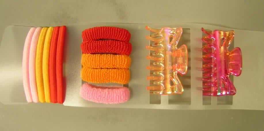 Haarklammern aus Kunststoff in Form einer Warenzusammenstellung in Aufmachung für den Einzelverkauf, sog. "Haaraccesoire, Artikel-Nr. 08-7485 S/13".
Die Warenzusammenstelleung besteht aus:
- zwei, ca. 6 cm großen Haarklammern aus orange-transparentem bzw. rot-transparentem Kunststoff in Form von zwei mittels einer Metallfeder verbundenen, zueinander gebogenen Kämmen,
- sechs ca. 0,5 mm dicken, rot-,orange- oder rosafarbenen Haargummis aus einem mit Spinnstoffgarnen umflochtenen, elastischem  Kautschukfaden, die an den Enden durch eine Hülse aus unedlem Metall zusammengefügt sind und
- fünf Haarbändern mit einem Durchmesser von ca. 1,5 cm, aus elastischen, schlauchförmigen Schlingengewirken aus rot-,orange-, oder rosafarbenen Spinnstoffen, lediglich geschnitten.
Die Haargummis bestimmen aufgrund des Umfangs, die Haarklammern aufgrund ihres Wertes den Charakter der Warenzusammenstellung, so dass die Einreihung in die zuletzt genannte der gleichermaßen in Betracht kommenden Positionen erfolgt. 
Die Erzeugnisse sind auf einer Pappkarte mit Aufhängeöse in einer transparenten Kunststofftüte für den Einzelverkauf aufgemacht.
Ein Bild der Ware befindet sich im Internet unter http://ec.europa.eu/taxation_customs/dds/ebticau_de.htm.