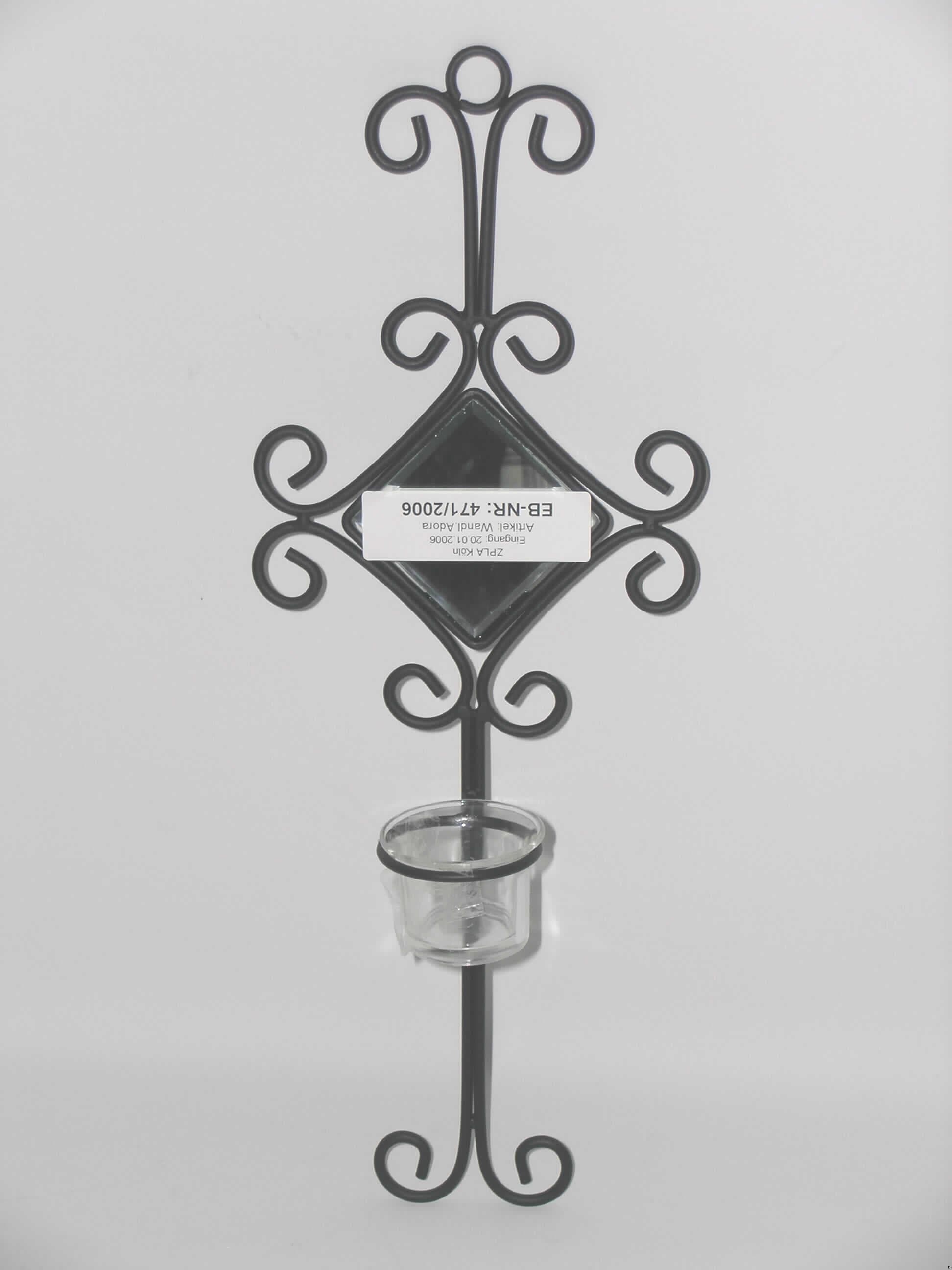 Nichtelektrischer Beleuchtungskörper, anderweit weder genannt noch inbegriffen, sog. Wandl. Adora, Artikel-Nr. 26180005LT211, bestehend aus einem ca. 47 cm großen aus Metallstäben zusammengeschweißten Wandhalter mit gebogenen Enden. Im oberen Teil befindet sich eine quadratische Öffnung (Kantelänge ca. 7,5 cm), in der ein spiegelnder Glaseinsatz eingeklebt ist. Darunter befindet sich ein Ring, der als Halter für ein farbloses  Glasgefäß dient. Das 4,5 cm hohe Glasgefäß mit nach außen gewölbtem Rand hat einen Innendurchmesser von 3,7 cm und ist passgenau für ein handelsübliches Teelicht gearbeitet. Der Halter ist mit einer Aufhängeöse versehen.

Abbildung der Ware im Internet.