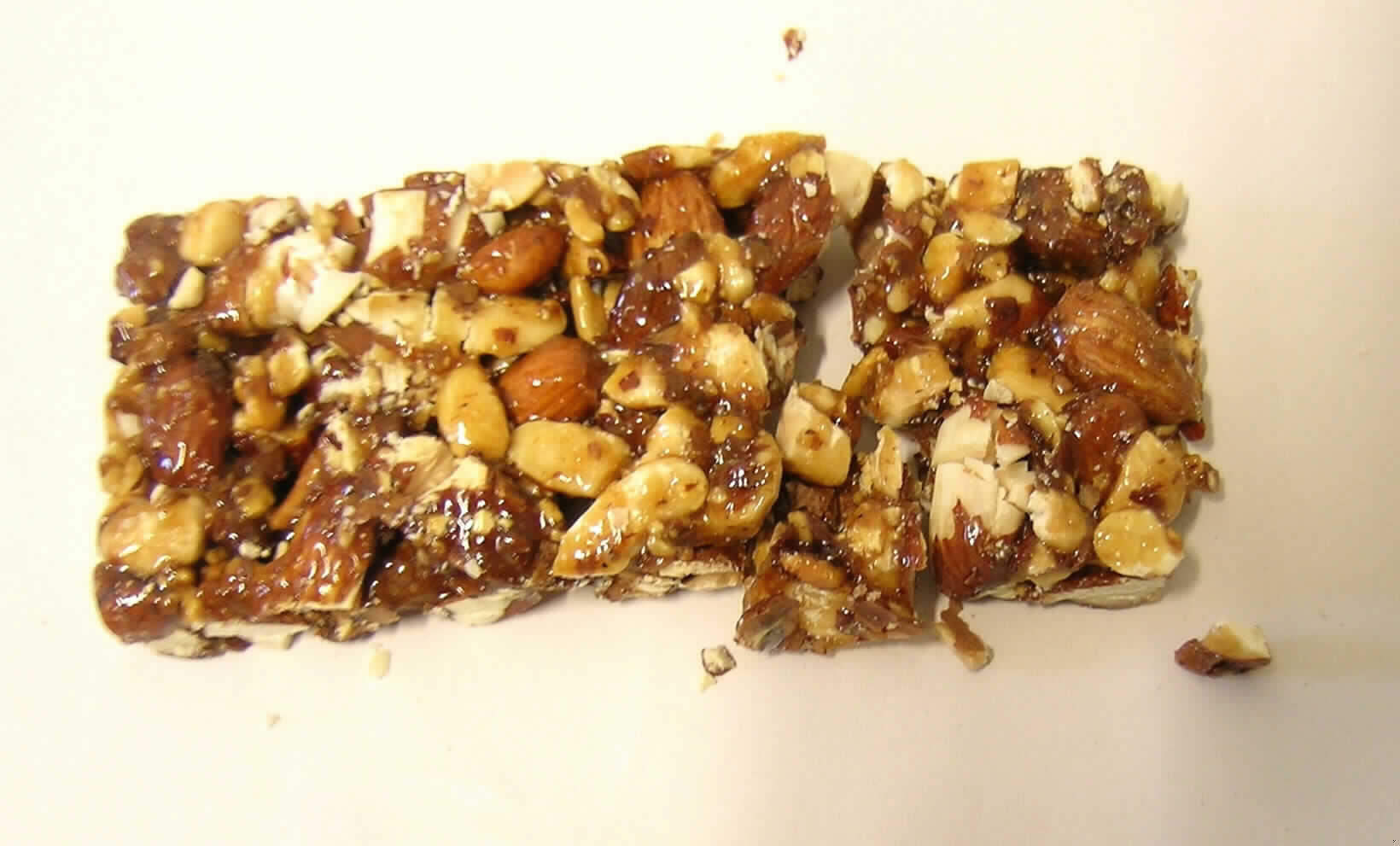 Mandelriegel.

Antragsangaben (als zutreffend unterstellt): Krokant mit Mandel, Zutaten: Mandeln, Zucker, Glucose.

Untersuchungsergebnis der vorgelegten Warenprobe: ca. 10x4,5x1 cm großer Riegel aus teilweise zerkleinerten Mandeln, welche mit einer braunen Krokantschicht überzogen sind. Geschmack: süß, nach karamellisierten Mandeln, knusprig. Verpackung: einzeln in etikettierter Schlauchfolie verpackt, auszugsweise: "Nettogewicht 40 g, Saccharose: 24,4 g/100 g";  ermittelter Mandelanteil: ca. 76 GHT.

Geröstete Mandeln, in anderer Weise zubereitet oder haltbar gemacht, in unmittelbaren Umschließungen mit einem Gewicht des Inhalts von 1 kg oder weniger.
