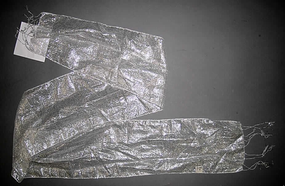 Schal, sog. Sommerschal, siehe Foto,
- aus 0,3 mm dicken, durchscheinenden, buntgewebten Geweben aus laut Antrag überwiegend 
  Viskose (künstliche Chemiefasern), laut ergänzenden Antragsangaben mit einer Beimischung 
  von Metallgarnen (Spinnstoffe der Position 5605),
- rechteckig, in den Abmessungen: 178 cm x 18 cm,
- an allen Rändern durch Umschlagen und Festnähen gesäumt (somit konfektioniert),
- an den Schmalseiten mit 12 cm langen, geknoteten Fransen ausgestattet,
- nicht handgearbeitet.