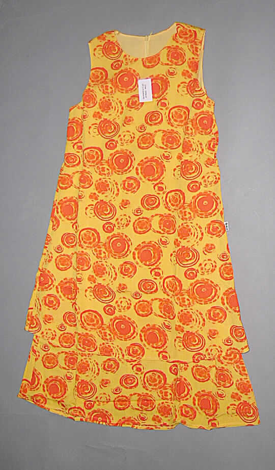 Kleid für Mädchen, sog. Volantkleid, Artikel-Nr. 592529, Größe 140 / 146, siehe Abbildung; 
- aus 0,4 mm dicken, maschinell bedruckten Geweben aus lt. Antrag 100 % Viskose 
  (künstliche Chemiefasern),
- mit einem runden, halsnahen Ausschnitt, 
- ärmellos,
- im Rückenteil mit einer Öffnung mit Reißverschluss,
- wadenlang (Rückenlänge: 95 cm), kann somit aufgrund der Länge ohne ein
  weiteres, den Unterkörper bedeckendes Kleidungsstück als Kleid getragen werden,
- als Stufenkleid mit einem am Futter angenähten Volant gearbeitet,
- an den Abschlüssen gesäumt.