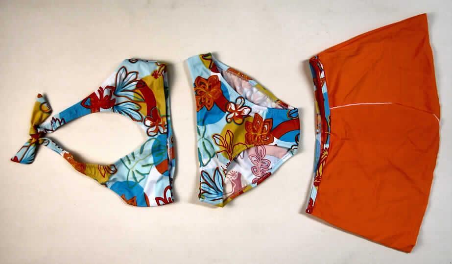 Zusammenstellung von Kleidungsstücken für Mädchen, bestehend aus einem zweiteiligen Badeanzug (Bikini) und einem Rock, sog. Bikini mit Rock, Größe 128, siehe Foto,
- aus bis zu 0,7 mm dicken, einfarbigen und bunt bedruckten Gewirken aus laut Antrag 80% Polyamid und 20%
  Elasthan (Elastomergarne; beides synthetische Chemiefasern); ohne Kautschukfäden, die Elastizität ergibt sich aus der
  Verwendung der Elastomergarne,
-Rock:
-- soll laut Antragsangaben ausschließlich als Badekleidung getragen werden,
-- über den Schritt reichend (Seitenlänge: 21 cm),
-- ungefüttert,
-- in der Taille abschließend, mit einem elastischen, bunt bedruckten Taillenbund,
-- vorn mit einer Überlappung in der Art eines Wickelrocks; ohne Öffnung oder Verschluss,
-- an allen Rändern gesäumt.
