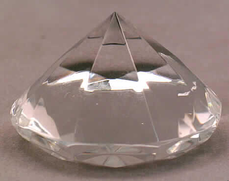 Nachahmung von Edelsteinen, sog. Glas-Deko-Diamant, siehe Foto, 
- Diamant aus Glas,
- mit einem Durchmesser von ca. 5,5 cm und einer Höhe von ca. 3,3 cm, 
- mit Diamantschliff (Achtkant), 
- geschliffen und mechanisch poliert (lt. Antragsangaben).