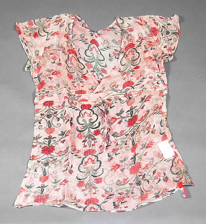 Bluse für Frauen, sog. Tunic, Art. Nr. 7840-4424-200, Größe S, siehe beigefügtes Foto,
- aus 0,2 mm dicken, buntbedruckten, durchscheinenden Geweben aus lt. Antrag 100%
  Seide,
- über die Taille reichend (Rückenlänge: 63 cm),
- mit einem sehr tiefen, V-förmigen Halsausschnitt mit nicht festgenähter Randeinfassung mit
  Überlappung von links auf rechts; ohne Öffnung und ohne Verschluss,
- unterhalb der Brust mit einem eingearbeiteten Bindeband, welches vorn in der Mitte
  gebunden wird und dadurch die Büste anatomisch der weiblichen Körperform entsprechend 
  formt, aufgrund der Gestaltung des Brustbereichs erkennbar Frauenkleidung,
- mit kurzen Ärmeln,
- am unteren Rand durch Umschlagen und Festnähen gesäumt,
- erfüllt aufgrund der Gewebedicke, des Schnitts und der Ausstattung die Bedingungen zur
  Einreihung als Bluse.