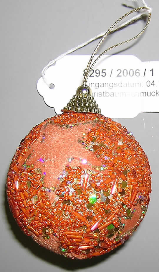Erzeugnis aus Glaskurzwaren, sog. Hänger "Kugel DANA", Art. 69704, siehe Foto,
- in Form einer Kugel mit Aufhängeschlaufe mit einem Durchmesser von ca. 7 cm,
- mit einem formgebenden Korpus aus Kunststoff (Styropor), von dem keine Zierwirkung
  ausgeht; vollständig mit kleinen Partikeln aus Kunststoff überzogen,
- mit orangefarbenen, durchbohrten Glasperlen mit einem Durchmesser von jeweils ca. 2 mm
  in Form von Körnern mit einer Länge von ca. 2 mm sowie in Form von Röhrchen mit einer 
  Länge von ca. 7 mm beklebt (außer im Bereich der sternförmigen Spinnstoffzuschnitte),
- mit sechs Zuschnitten aus gerauten Gewirken aus Spinnstoffen in Form von fünfzackigen
  Sternen in unterschiedlichen Größen beklebt,
- Ränder der Spinnstoffsterne sind mit kleinen metallisierten Kunststoffplättchen eingefasst,
- zwischen den Glasperlen sind kleine, sechseckige Pailletten aus Kunststoff aufgeklebt,
- am oberen Ende mit einem aufgeklebten Krönchen aus Kunststoff mit einer dadurch 
  gezogenen Aufhängeschlaufe mit einer Länge von ca. 7 cm versehen,
- im Hinblick auf den Umfang an der Außenseite und dem äußeren Erscheinungsbild ist das
  Glas als charakterbestimmend anzusehen,
- keine Einreihung als Weihnachtsartikel in die Position 9505, da aufgrund der ganzjährigen
  Verwendbarkeit kein erkennbarer Bezug zur Advents- bzw. Weihnachtszeit gegeben ist.