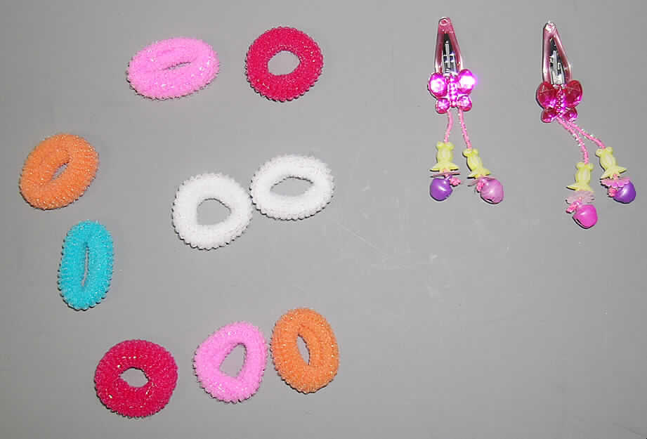 Warenzusammenstellung, bestehend aus 10 Haargummis aus Schlingengewirken und 
2 haarspangenähnlichen Clips aus Kunststoff, sog. Haarset Artikel FRINV-003074, siehe Foto,
- aufgemacht für den Einzelverkauf in einem einfach gearbeiteten, transparenten 
  Kunststoffbehältnis,
- zur Befriedigung eines speziellen Bedarfs zusammengestellt (zum Zusammenhalten des
  Haaares),
- 10 Haarbänder aus einfarbigen, elastischen, schlauchförmigen Schlingengewirken aus 
  synthetischen Chemiefasern, nur geschnitten, nicht konfektioniert:
- - mit einem Durchmesser von ca. 3,0 cm und einer Breite von ca. 1,0 cm,
- 2 haarspangenähnlichen Clips aus Kunststoff: ca. 3,0 cm groß; in Form von zwei mittels
  einer Feder aus unedlem Metall verbundenen Kämmen mit einander zugebogenen Zinken
  aus Kunststoff,
- insbesondere nach der Menge und dem Wert verleihen die Haarbänder aus 
  Schlingengewirken 
  der Warenzusammenstellung ihren wesentlichen Charakter.