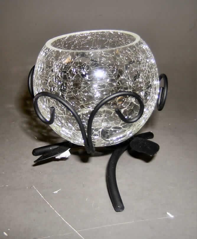 Ziergegenstand aus Glas, sog. "Teelichthalter, Art.-Nr.: 880431", siehe Foto, 
- zusammengesetzte Ware, bestehend aus
- gewöhnlichem, ungefärbtem Glas mit Bruchstruktur in Form eines bauchigen Gefäßes,
- - mit einem Durchmesser (oben) von ca. 5,5 cm und einer Höhe von ca. 6,5 cm,
- - augenscheinlich mechanisch gefertigt,
- unedlem Metall (schwarz lackierter Eisendraht) in Form eines ornamentartigen Gestells,
- - mit einer Höhe von ca. 7 cm, passgenau für das Glasgefäß,
- das Glas bestimmt im Hinblick auf den Wert, die Verwendung und das äußere 
  Erscheinungsbild den Charakter der zusammengesetzten Ware,
- kein nichtelektrischer Beleuchtungskörper der Pos. 9405, weil das Glasgefäß u.a.
  keine passgenaue Aufnahmevorrichtung für ein Teelicht aufweist.