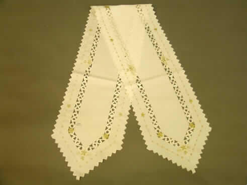Tischwäsche (Tischband), siehe Foto,
- rechteckig, an den Schmalseiten spitz zu laufend,
- in den Abmessungen: 170 cm x 28 cm,
- aus 0,4 mm dicken, einfarbigen Geweben aus lt. Antrag 100% synthetischen 
  Chemiefasern, 
- an den zackig geschnittenen Rändern gesäumt, somit konfektioniert,
- mit verschiedenfarbigen, nicht erhabenen Applikationsstickereien; teilweise durchbrochen 
  durch Ausschneiden von Teilen des Gewebes,
- wird üblicherweise regelmäßig gewaschen und kennzeichnet sich nach Material,
  Ausstattung und Verwendungszweck als Tischwäsche (Tischband), somit keine Ware zur
  Innenausstattung (Zierdecke) im Sinne der Position 6304
- kein Festartikel der Position 9505, da die Ware einen eigenen Verwendungszweck hat.