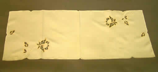 Tischwäsche (Tischläufer), sog. Tischläufer mit Lochstickerei, siehe Foto,
- rechteckig, in den Abmessungen: 109 cm x 39 cm,
- aus 0,4 mm dicken, einfarbigen Geweben aus lt. Antrag 100% synthetischen 
  Chemiefasern, 
- an den Rändern gesäumt, somit konfektioniert,
- mit verschiedenfarbigen, nicht erhabenen Applikationsstickereien; teilweise durchbrochen 
  durch Ausschneiden von Teilen des Gewebes,
- wird üblicherweise regelmäßig gewaschen und kennzeichnet sich nach Material,
  Ausstattung und Verwendungszweck als Tischwäsche (Deckchen), somit keine Ware zur
  Innenausstattung (Zierdecke) im Sinne der Position 6304.