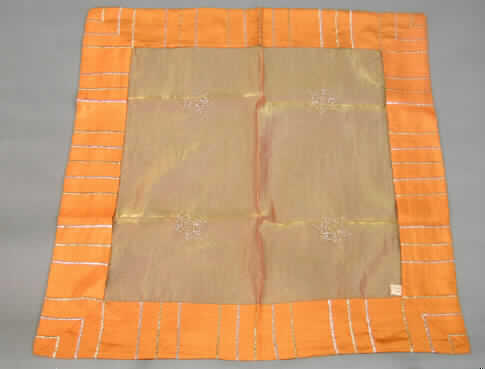 Tischwäsche (Mitteldecke), sog. Tischdecke Organza, siehe Foto,
- quadratisch, in den Abmessungen: ca. 85 cm x 85 cm,
- aus 0,1 mm dicken, einfarbigen, durchscheinenden Geweben (sog. Organza), 
  am Rand doppelt gearbeitet durch einen aufgenähten, 11,5 cm breiten Streifen 
  aus flachen Stickereien der Pos. 5810 mit einem Stickgrund aus 0,3 mm dicken, 
  einfarbigen Geweben; alle Flächenerzeugnisse aus lt. Antrag 
  100% synthetischen Chemiefasern,
- durch Zusammennähen konfektioniert,
- in der Mitte mit verschiedenfarbigen, aufgestickten Motiven (Sterne),
- wird üblicherweise regelmäßig gewaschen und kennzeichnet sich nach Material,
  Ausstattung und Verwendungszweck als Tischwäsche (Deckchen), somit keine Ware 
  zur Innenausstattung (Zierdecke) im Sinne der Position 6304,
- kein Festartikel der Position 9505, da die Ware einen eigenen Verwendungszweck hat.
