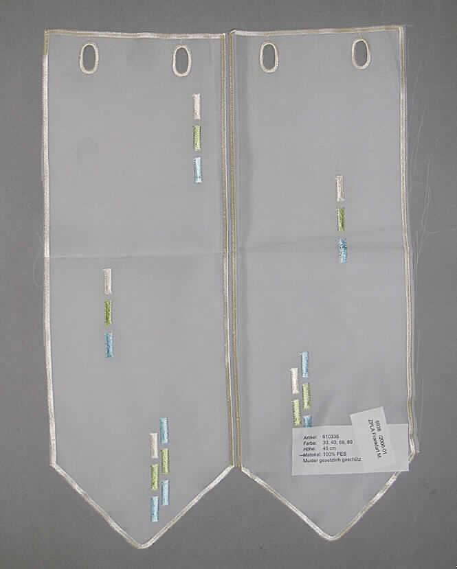 Gardine aus Stickerei, sog. Panneaux, Art. 610335, siehe Foto
- aus Stickerei der Position 5810 mit Stickgrund aus durchscheinenden, lichtdurchlässigem 
  Geweben aus lt. Antrag 100 % Polyester (synthetische Chemiefasern),
- als Meterware auf Rollen (etwa 19 m), mit einer Höhe von bis zu 45 cm,
- mit aufgesticktem, grafischem Muster,
- am oberen Rand mit eingearbeiteten Öffnungen zum Einschieben einer Gardinenstange, 
  somit liegt mehr als ein Gardinenstoff (Stickerei als Streifen der Position 5810) vor,
- am unteren Rand spitz zugeschnitten,
- durch Zuschneiden konfektioniert.
