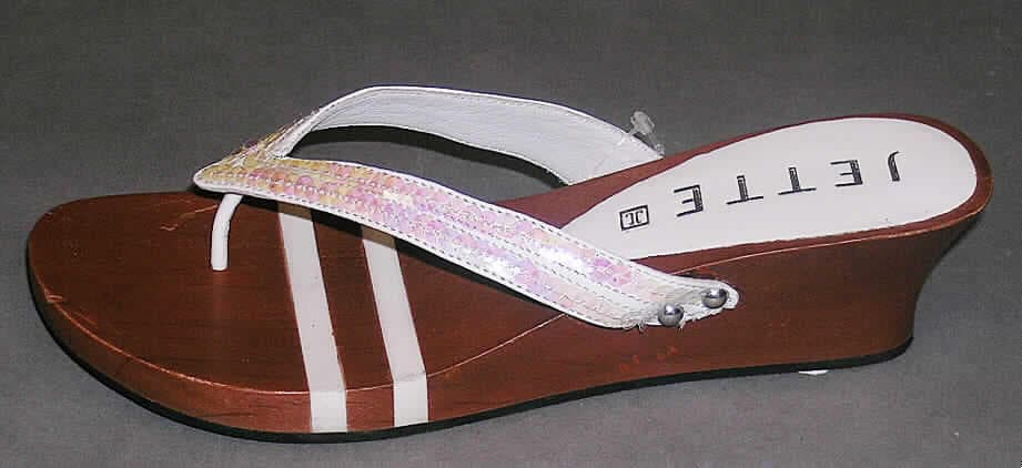 Freizeitschuhe (siehe Foto)
- mit Laufsohlen aus Kunststoff (Stoff, der die Berührungsfläche mit dem Boden bildet),
- mit einer Hauptsohle aus Holz,
- ohne Innensohle,
- ohne Metallschutz in der Vorderkappe,
- mit Oberteil aus Lederriemen,
- auf das Oberteil sind großflächig Pailetten als Verzierung aufgenäht,
- nicht handgearbeitet