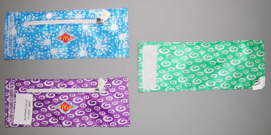 Anderes Behältnis, sog. Handgelenktasche ("Mc Donald's - Throw'n Go 2007"), siehe Foto, 
- mit einer Außenseite aus Spinnstoffen, 
- mit den Abmessungen von ca. 21 (L) x 8 (B) cm (flachliegend), 
- mittels Klettverschluss am Handgelenk zu befestigen, 
- auf der die Vorderseite bildenden Seite mit dem aufgedruckten Mc Donald's Emblem, 
- mit einem über die Längseite verlaufenden Reißverschluss zu öffnen, 
- innen ohne weitere Unterteilung, nicht gefüttert, 
- augenscheinlich nicht handgearbeitet.