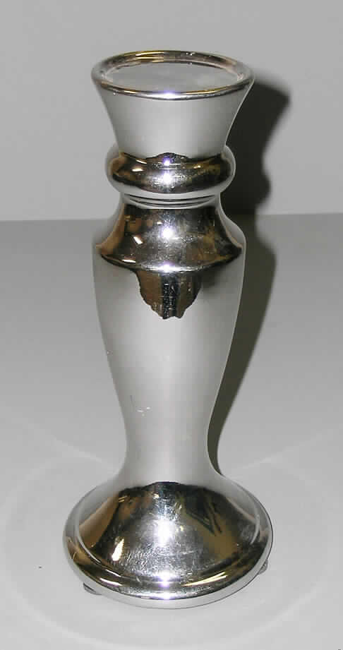 Keramischer Ziergegenstand, sog. Kerzenhalter, siehe Foto, 
- in Form eines amphorenförmigen, silber glasierten Ständers, 
- mit einem max. Durchmesser von ca. 11 cm (Stellfläche) und einer Höhe von ca. 26 cm, 
- oben mit einer Abstellfläche mit leicht nach oben gezogenem Rand (Durchmesser ca. 7 
  cm) zum Abstellen einer Kerze (nicht Gegenstand dieser vZTA), 
- keramisches Erzeugnis, nach der Formgebung gebrannt, tonmineralhaltiges Material 
  enthaltend, 
- nach augenscheinlicher Untersuchung handelt es sich um Steingut (hellcremefarbener 
  Scherben, inhomogene Bestandteile mit bloßem Auge nicht erkennbar, nicht durch- 
  scheinend, mit einem Stahlnagel ritzbar, an der Zunge haftend), 
- augenscheinlich nicht handgearbeitet, 
- kein nichtelektrischer Beleuchtungskörper der Position 9405, weil die Ware keinen her- 
  kömmlichen Beleuchtungskörper darstellt und keine spezielle Vorrichtung zur Aufnahme
  einer Kerze aufweist, die der Kerze einen festen Halt gibt (Klammer, Dorn, passgenaue
  Vorrichtung usw.).