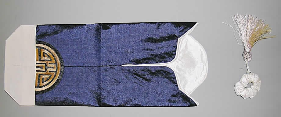 Zweiteilige Zusammenstellung von konfektionierten Spinnstoffwaren, bestehend aus einem  Verpackungsbeutel und einer elastischen Verschlussvorrichtung, Art. A30-x0080, siehe Foto; durch Zusammennähen zugeschnittener Teile konfektioniert; nicht handgearbeitet,
- Verpackungsbeutel:
- - in den Abmessungen: ca. 15 cm x 37 cm (flachliegend), 
- - aus verschiedenen, 0,3 mm dicken, einfarbigen Geweben aus lt. Antrag Viskose 
   (künstliche Chemiefasern),
- - im oberen Bereich mit kontrastfarbenen Gewebezuschnitten doppelt gearbeitet,
- - vom oberen, bogenförmig gearbeiteten Rand ausgehend mit einer ca. 10 cm langen 
    schlitzförmigen Öffnung, so dass der obere Teil des Beutels wie ein Kragen umgelegt 
    werden kann,
- - mit einer großflächigen Applikationsstickerei verziert,
- Verschlussvorrichtung:
- - aus einem elastischen Band mit einem Durchmesser von ca. 2 cm gefertigt; mit
    Zuschnitten aus einfarbigen Geweben aus Chemiefasern umhüllt und mit einer Quaste 
    dekoriert,
- dient z. B. zur Aufnahme von Flaschen und Vasen,
- stellt sich nicht als Beutel zu Verpackungszwecken der Position 6305 dar, da dieser nicht 
  zum Transport oder zur Lagerung der verpackten Ware bis zum Verkauf dient,
- wird nach Gesamtbeschaffenheit und Verarbeitung auch nicht vom Warenkreis der Posi- 
  tion 4202 erfasst.