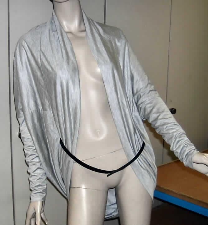 Zweiteilige Warenzusammenstellung, bestehend aus einem strickjackenähnlichen Kleidungsstück und einem Gürtel, sog. Westenähnliche Bekleidung (Modell 120002/83023), Größe 36, siehe Fotos,
- gemeinsam für den Einzelverkauf aufgemacht und zur Befriedigung eines speziellen Bedarfs zusammengestellt,
- strickjackenähnliche Kleidung (nach Wert und Umfang charakterbestimmend):
-- aus 0,6 mm dicken, melierten Gewirken aus lt. Antrag 81% Viskose und 19% Polyester (künstliche und 
   synthetische Chemiefasern), 
-- über den Schritt reichend (Rückenlänge: 77 cm in getragenem Zustand),
-- vorn mit einer durchgehenden Öffnung ohne Verschluss, u. a. deshalb keine Hemdbluse der Position 6106,
-- ohne Merkmale, die auf den Trägerkreis schließen lassen (unisex),
-- mit langen Ärmeln, an den Abschlüssen gesäumt,
-- in den Seitennähten mit kleinen Öffnungen, durch die der Gürtel gezogen wird,
-- der Hauptkörper ist stark gerundet und an allen Rändern mit einem 14 cm breiten, doppelt gearbeiteten 
   Abschluss ausgestattet,
- Gürtel (Bekleidungszubehör):
-- aus ca. 3,5 mm dickem Leder,
-- 95 cm lang und 1,5 cm breit,
-- an einem Ende mit drei ausgestanzten Löchern, am anderen Ende mit einem Metalldorn ausgestattet.