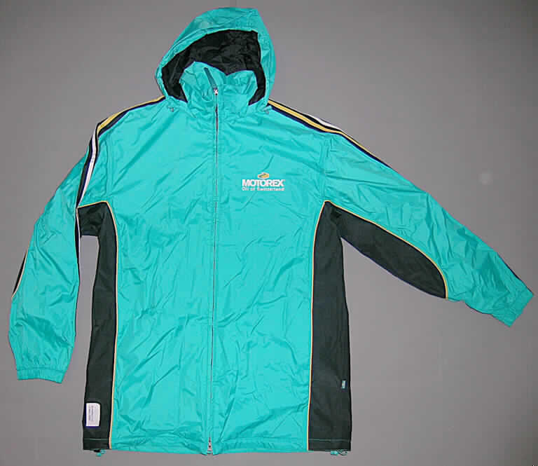 Blouson aus Geweben der Position 5903, sog. Textilie, Größe M, siehe Abbildung;
- aus verschiedenen einfarbigen, 0,2 mm dicken, einseitig (Innenseite) mit Kunststoff (lt. 
  ergänzenden Antragsangaben: Polyurethan; kein Zellkunststoff) bestrichenen 
  Geweben (türkis) bzw. mit einer geprägten Kunststofffolie überzogenen Geweben 
  (schwarz) der Position 5903, 
- über den Schritt reichend (Rückenlänge: 80 cm),
- mit einem Stehkragen, in den eine Kapuze integriert ist,
- vorn mit einer durchgehenden Öffnung mit Reißverschluss, ohne Überlappung; 
  ohne Merkmale, die auf einen bestimmten Trägerkreis (Männer oder Frauen) 
  hinweisen (unisex),
- mit langen Ärmeln, die über den unteren Rand des Kleidungsstückes
  hinausreichen; an den Ärmelenden mit elastischen, verengenden Abschlüssen;
  auf den Ärmeln mit aufgesetzten, kontrastfarbenen Streifen,
- seitlich mit zwei eingesetzten Taschen mit Reißverschluss,
- im Rückenteil unterhalb der Taille mit einer eingesetzten Tasche mit Reißverschluss,
- mit einem netzartigen, durchbrochenen Futter,
- im Vorder- und Rückenteil mit kontrastfarbenen Paspeln,
- am unteren Rand durch einen elastischen Tunnelzug zu verengen.