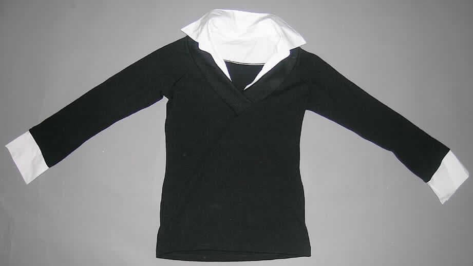 Hemdbluse für Frauen, sog. Pullover (Art. 229317, Emi), Erwachsenengröße, siehe Foto,
- charakterbestimmend aus 1,4 mm dicken, nicht leichten, einfarbigen Gewirken aus lt.
  Antrag 90 % Polyacryl und 10 % Elasthan (beides synthetische Chemiefasern); mit 12
  Maschen in vertikaler und 8 Maschen in horizontaler Richtung je linearen Zentimeter,
- Krageneinsatz und Ärmelabschlüsse aus einfarbigen Geweben; durch die Gestaltung des
  Kragenbereichs und der Ärmel soll der optische Eindruck vermittelt werden, dass eine
  langärmelige Hemdbluse unter einem Pullover getragen wird,
- über die Taille reichend (Rückenlänge: 63 cm),
- mit einem Umlegekragen (u.a. deshalb keine Ware der Position 6109),
- vorne mit einer kurzen Öffnung mit Überlappung von rechts auf links (Frauenkleidung),
- mit langen Ärmeln,
- am unteren Rand durch Umschlagen und Festnähen gesäumt,
- den Hemden für Männer entsprechend zugeschnitten,
- erfüllt aufgrund des Schnitts, der Art und der Maschenzahl des Gewirkes die Bedingungen
  zur Einreihung als Hemdbluse, daher kein Pullover der Position 6110.
