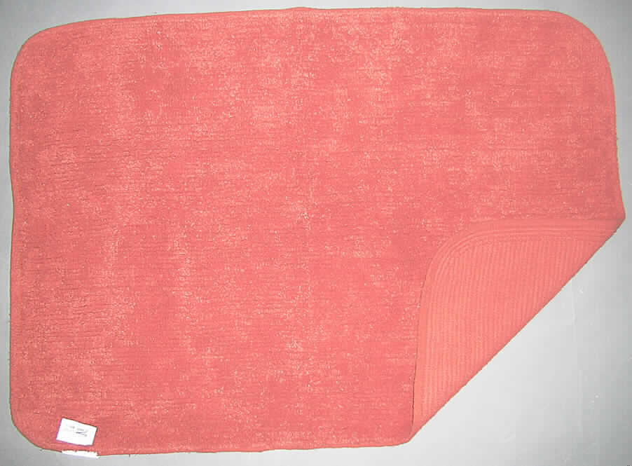 Badevorleger/Teppich (lt. Antrag: "Badeteppich aus 100% Baumwolle Kat. 3862, Farbe: rost", siehe Foto)
- mit den Abmessungen (flachliegend) von ca. 90 x 60 cm,
- getuftet (Nadelflor); in einen textilen, gewebten Grund ist nachträglich ein ca. 0,8 cm hoher 
  Flor aus (lt. Antrag) Baumwolle eingezogen worden,
- an den Rändern gesäumt (= konfektioniert); mit einem etwa 1 cm breiten florlosen 
  Rand (deshalb keine Fliese),
- kennzeichnet sich durch seine Festigkeit, Dicke und Steifheit als Fußbodenbelag