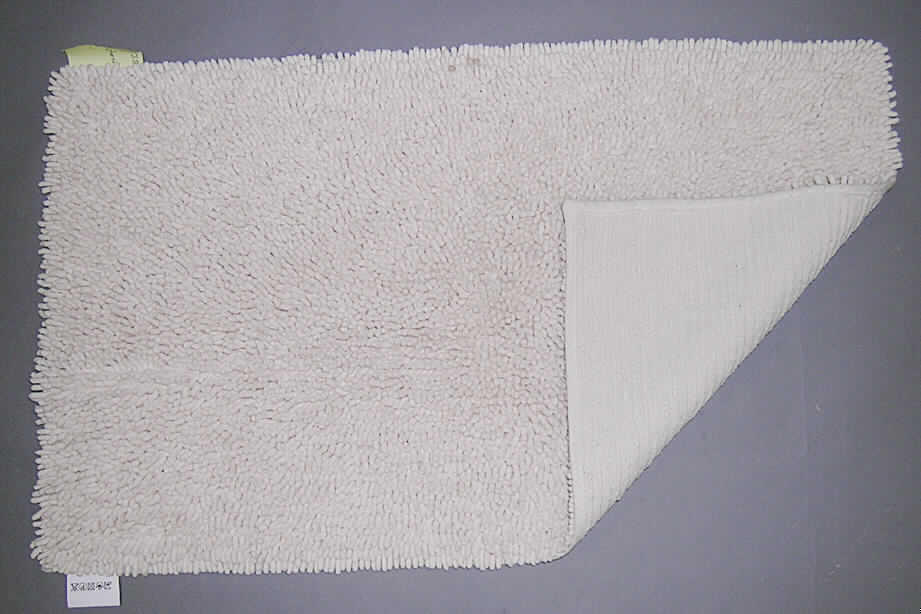 Badevorleger/Teppich (lt. Antrag: "Badeteppich aus 100% Baumwolle Kat. 3861, Farbe: beige", siehe Foto)
- mit den Abmessungen (flachliegend) von ca. 80 x 50 cm,
- getuftet (Nadelflor); in einen textilen, gewebten Grund ist nachträglich ein ca. 0,8 cm hoher 
  Flor aus (lt. Antrag) Baumwolle eingezogen worden,
- an den Rändern gesäumt (= konfektioniert); mit einem etwa 1 cm breiten florlosen 
  Rand (deshalb keine Fliese),
- kennzeichnet sich durch seine Festigkeit, Dicke und Steifheit als Fußbodenbelag