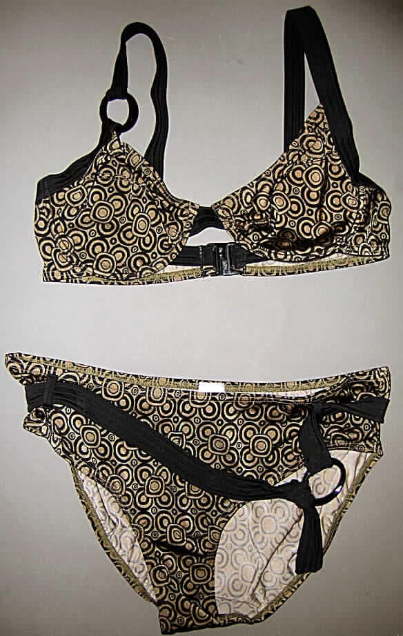 Zweiteiliger Badeanzug (Bikini) für Frauen, Art. 80601, Größe 42/42B, siehe Foto
- aus 0,7 mm dicken, buntbedruckten Gewirken aus lt. Antrag 80 % Polyamid
  und 20 % Elasthan (Elastomergarn, beides synthetische Chemiefasern),
- ohne Kautschukfäden; die Elastizität ergibt sich durch die Verwendung von 
  Elastomergarnen (Elasthan),
- Oberteil: 
-- die Brust bedeckend; mit einzeln ausgearbeiteten Büstenteilen; mit eingearbeiteten 
   Formbügeln,
-- mit einem für Bikinioberteile typischen Kunststoffverschluss im Rücken,
-- mit etwa 2 cm breiten Trägern über den Schultern, als Verbindung zwischen dem 
   rechten Büstenteil und dem rechten Träger ist ein ovaler Ring aus Kunststoff eingenäht,
-- ist dazu bestimmt als Oberteil eines zweiteiligen Badeanzugs (Bikini) sichtbar als 
   Oberkleidung getragen zu werden, stellt somit keinen Büstenhalter der Position 6212 dar, 
- Hose: 
-- in Form eines Hüftslips gearbeitet,
-- mit hohen Beinausschnitten,
-- am oberen Rand mit aufgenähten Gürtelschlaufen und mit einem durchgezogenen
   Bindegürtel, an dessen einen Ende ein ovaler Ring aus Kunststoff angenäht ist,
-- im Schritt mit einer für Badekleidung typischen Hygieneeinlage,
-- aufgrund des Schnitts erkennbar als Frauenkleidung,
- die Kleidungsstücke lassen nach Schnitt, Ausstattung und Material erkennen, dass 
  sie ausschließlich oder hauptsächlich dazu bestimmt sind, als Badekleidung getragen zu 
  werden.