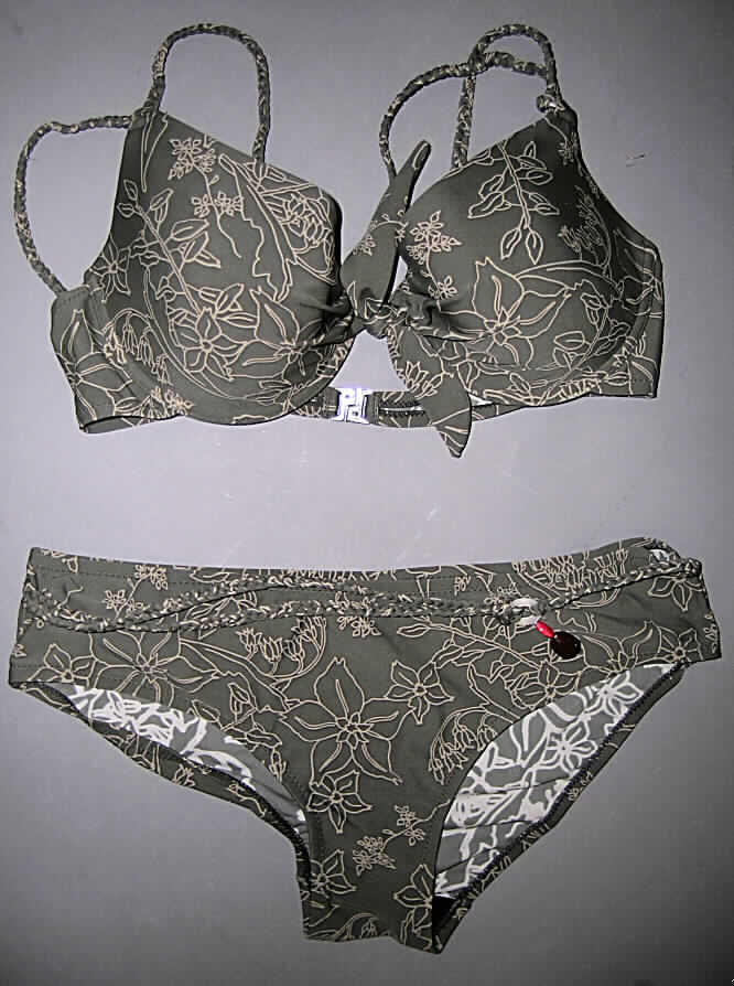 Zweiteiliger Badeanzug (Bikini) für Frauen, Art. 80701, Größe 40/40C, siehe Foto
- aus 0,7 mm dicken, bedruckten Gewirken aus lt. Antrag 80 % Polyamid und 20 % Elasthan 
  (Elastomergarn, beides synthetische Chemiefasern),
- ohne Kautschukfäden; die Elastizität ergibt sich durch die Verwendung von 
  Elastomergarnen (Elasthan),
- Oberteil: 
-- die Brust bedeckend; mit einzeln ausgearbeiteten, gepolsteren Büstenteilen; mit 
   eingearbeiteten Formbügeln; zwischen den Büstenteilen mit einem zusätzlich angenähten
   kleinen Gewirkezuschnitt, der verknotet optisch den Eindruck erweckt, als ob die
   beiden Büstenteile lediglich durch diesen Knoten zusammengehalten werden,
-- mit einem für Bikinioberteile typischen Kunststoffverschluss im Rücken,
-- mit je zwei schmalen, geflochtenen Trägern über den Schultern, als Verbindung zwischen 
   den Büstenteilen und den Trägern ist je in kleiner Ring aus Kunststoff eingenäht,
-- ist dazu bestimmt als Oberteil eines zweiteiligen Badeanzugs (Bikini) sichtbar als 
   Oberkleidung getragen zu werden, stellt somit keinen Büstenhalter der Position 6212 dar, 
- Hose: 
-- in Form eines Hüftslips gearbeitet, 
-- vorn mit zwei in den Seiten vernähten, lose hängenden, gflochteten Bändern aus dem
   Gewirke der Hose, die durch einen Ring aus Kunststoff verbunden sind und zusätzlich 
   mit zwei stilisierten, farbigen Steinen aus Kunststoff verziert sind,
-- im Schritt mit einer für Badekleidung typischen Hygieneeinlage,
-- aufgrund des Schnitts erkennbar als Frauenkleidung,
- die Kleidungsstücke lassen nach Schnitt, Ausstattung und Material erkennen, dass 
  sie ausschließlich oder hauptsächlich dazu bestimmt sind, als Badekleidung getragen zu 
  werden.
