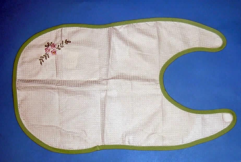 Bekleidungszubehör, sog. Seniorenlätzchen mit Klettverschluss, in Einheitsgröße, siehe Foto,
- in annähernd rechteckiger Form mit abgerundeten Ecken,
- aus 0,6 mm dicken, einfarbigen Geweben (Waffelmuster) aus laut Antrag Baumwolle,
- im oberen Drittel mit einer etwa U-förmigen Öffnung; an dieser Schmalseite offen gearbeitet 
  und mit einem Klettverschluss (im Nacken) zu schließen, 
- an allen Rändern mit einem schmalen Gewebestreifen eingefasst (somit konfektioniert),
- auf der Schauseite mit einer Applikationsstickerei verziert,
- dient dem Schutz der Kleidung beim Essen,
- nicht handgearbeitet.