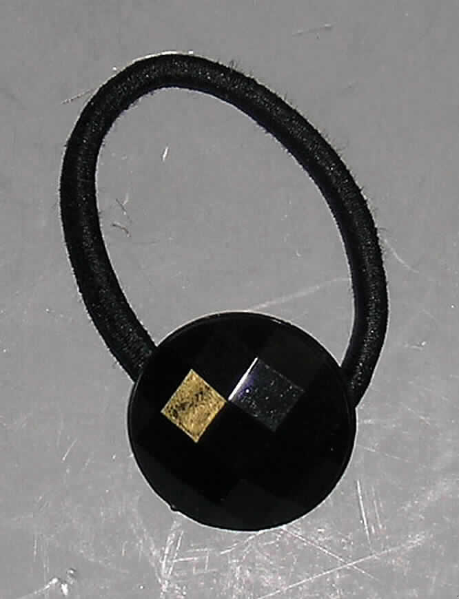 Anderes konfektioniertes Bekleidungszubehör, sog. Haargummi mit Plastikknopf, 
Art. TKI070831, siehe Foto
- bestehend aus einer elastischen Kordel aus einem Kautschukfaden, der mit einfarbigen 
  Spinnstoffgarnen umflochten ist (Meterware der Position 5604),
- mit einem Durchmesser von etwa 4 cm und einer Dicke von etwa 3,5 mm,
- auf die Kordel ist ein facettenartig gestalteter Knopf aus Kunststoff (Durchmesser etwa
  2,5 cm)  aufgezogen, die beiden Enden der gummielastischen Kordel sind in einem Art 
  Tunnel auf der Rückseite des Knopfes zusammengeführt und durch Kleben befestigt 
  (damit konfektioniert),
- soll als Haargummi zum Zusammenhalten des Haares (z.B. Zopf / Pferdeschwanz) dienen,
- der Spinnstoff bestimmt im Hinblick auf die Verwendung als Haargummi den Charakter der 
  Ware, der Kunststoff ist in Bezug auf das äußere Erscheinungsbild (Verzierung) als 
  charakterbestimmend anzusehen, somit kann keinem der beiden Stoffe (Spinnstoff / 
  Kunststoff) eine charakterbestimmende Eigenschaft zuerkannt werden; die Ware ist damit 
  der von den gleichermaßen in Betracht kommenden Positionen (3926 und 6217) in der 
  Nomenklatur zuletzt genannten zuzuweisen,
- in Anbetracht des textilen Charakters wird die Ware nicht vom Warenkreis der Position
  9615 erfasst, kennzeichnet sich somit als konfektioniertes Bekleidungszubehör.