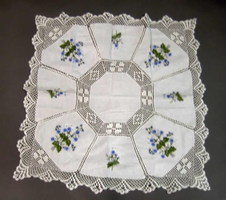 Tischwäsche, sog. Mitteldecke, Artikel 880530, siehe Foto,
- annähernd quadratisch; in den Abmessungen: ca. 82 cm x 82 cm,
- abgepasst hergestellt (konfektioniert),
- bestehend aus acht Zuschnitten aus flachen Stickereien (florale Motive) mit einem
  Stickgrund aus 0,4 mm dicken, einfarbigen Geweben, einem Zuschnitt aus nicht
  besticktem Gewebe sowie aus ca. 2,5 mm dicken, einfarbigen, gehäkelten Gewirken;
  alle laut Antrag aus 100% Baumwolle,
- die Mitte der Tischdecke bildet der Zuschnitt aus dem nicht bestickten Gewebe; 
  die Stickereien sind mit diesem Gewebe und auch untereinander durch die gehäkelten
  Gewirke verbunden, welche auch den bogenförmigen Rand der Tischdecke bilden,
- wird üblicherweise regelmäßig gewaschen und stellt sich somit als Tischwäsche dar
  (damit keine Ware zur Innenausstattung),
- im Bezug auf den Umfang sind die Gewebe bzw. Stickereien und die gehäkelten Gewirke 
  als annähernd gleichwertig anzusehen; im Bezug auf den Wert bestimmen die gehäkelten 
  Gewirke den Charakter der Ware.