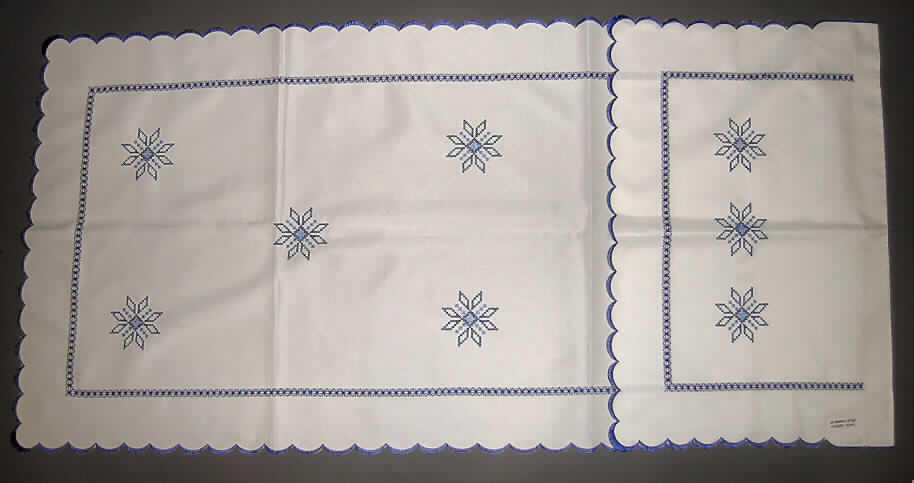 Ware zur Innenausstattung, sog. Überhandtuch, siehe beigefügte Abbildung,
- aus 0,4 mm dicken, Stickereien der Position 5810 mit Stickgrund aus Geweben aus lt. Antrag 100% Polyester (synthetische Chemiefasern),
- in den Abmessungen: etwa 58 cm breit und 119 cm lang; am oberen Rand mit einem etwa 35 cm 
  langen Umschlag (Gesamtlänge: 150 cm),
-- etwa 4 cm unterhalb des oberen Randes zusammengenäht, so dass eine Öffnung entsteht, durch die
   das sog. Überhandtuch auf eine Stange aufgefädelt wird und so eine dahinter angebrachte Hakenleiste, 
   an der z. B. Geschirrhandtücher aufgehängt werden können, verdeckt; stellt sich u. a. somit nicht als
   Vorhang der Position 6303 dar,
- an den bogigen Rändern gesäumt,
- kennzeichnet sich damit aufgrund der Ausstattung und insbesondere in Bezug auf den Verwendungszweck
  als Ware zur Innenausstattung der Position 6304.
