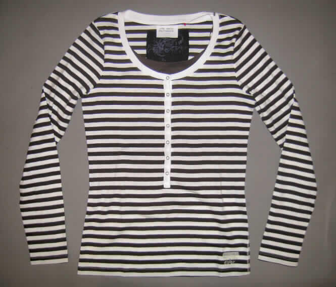 Modisches Unterhemd, sog. Damen T-Shirt, Größe M, siehe Foto,
- aus verschiedenen 0,9 mm dicken (somit leichten), einfarbigen und buntgewirkten Gewirken
  aus laut Antrag 100% Baumwolle,
- über die Taille reichend (Rückenlänge: 64 cm),
- vorn teilweise (von den Schultern bis unterhalb der Brust) doppelt gearbeitet, stellt sich
  insgesamt noch als leichtes Kleidungsstück dar,
- die obere, nicht die Halslinie bildende Lage weist eine kurze Öffnung mit Knöpfung von 
  rechts auf links auf; mit kontrastfarbener Randeinfassung,
- mit einem innen an den Schulter- und Seitennähten festgenähten, kontrastfarbenen
  Einsatz, der einen runden, halsfernen, aber nicht sehr tiefen Ausschnitt bildet,
- da der den Halsausschnitt bildende Rand keine Öffnung aufweist, handelt es sich nicht um
  eine Hemdbluse der Position 6106,
- mit langen Ärmeln,
- am unteren Rand gesäumt.
