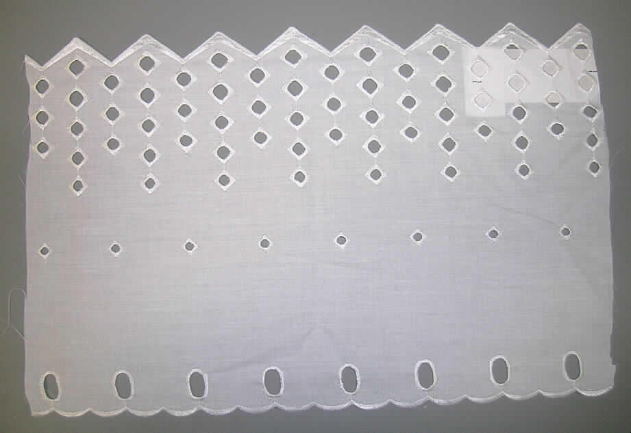 Gardine, sog. Panneaux, bestickt, Artikel 610243, siehe Abbildung;
- aus 0,2 mm dicker, maschinell hergestellter Loch-Stickerei der Position 5810 aus lt. Antrag 
  65% Polyester (synthetische Chemiefasern) und 35% Baumwolle, mit Stickgrund aus 
  durchscheinendem, lichtdurchlässigem Gewebe; aufgrund der Art des Flächenerzeugnisses 
  (durchscheinend, lichtdurchlässig) kein Vorhang der  Codenummer 6303 9290 90 0,
- Probenabschnitt in den Abmessungen: 28 cm hoch und 43 lang,
- am oberen Rand mit einem bogenförmigen Abschluss, 
- mit Löchern für die Gardinenstange,
- an den Schmalseiten geschnitten,
- am unteren Rand mit zackenartigen Abschlüssen (u.a. dadurch konfektioniert).