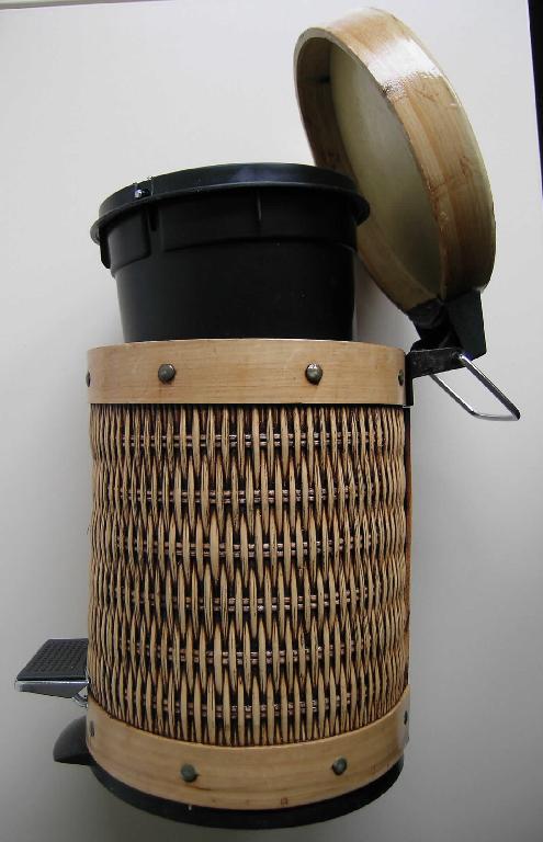 Aus verschiedenen Stoffen zusammengesetzte Ware in Form eines Treteimers (Fassungsvermögen 3 l, 26,5 cm groß, Durchmesser ca. 18,5 cm), bestehend aus einem formgebenden Korpus aus Holz, dessen Außenseite überwiegend mit einem Geflecht aus pflanzlichen Stoffen (lt. Angaben des Antragstellers aus Rattan) beklebt ist. Mit einem Fußpedal ist über ein Gestänge aus unedlem Metall der Deckel zu öffnen. Im Innern befindet sich ein ca. 19,5 cm hoher herausnehmbarer Eimer aus Kunststoff. 
Die Ware ist in einem bunt bedruckten Karton für den Einzelverkauf aufgemacht.
Da ein charakterverleihender Stoff nicht ermittelt werden kann, ist die Ware der zuletzt genannten, in Betracht kommenden Position zuzuweisen.