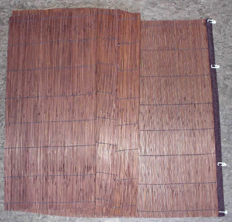 Bambus-Rollo 
- rechteckig (Abmessungen ca. 60 x 230 cm),
- charakterverleihend aus ca. 2 mm breiten, biegsamen Bambusstäbchen hergestellt, die
  durch Haltefäden aus Spinnstoffgarnen in Flächenform parallel aneinander gefügt sind,
- mit einem angenähten Gewebeband an der Oberseite verstärkt, das mit mehreren 
  Aufhängehaken aus Kunststoff versehen ist, 
- ohne Hinweise auf Fertigung in Handarbeit.