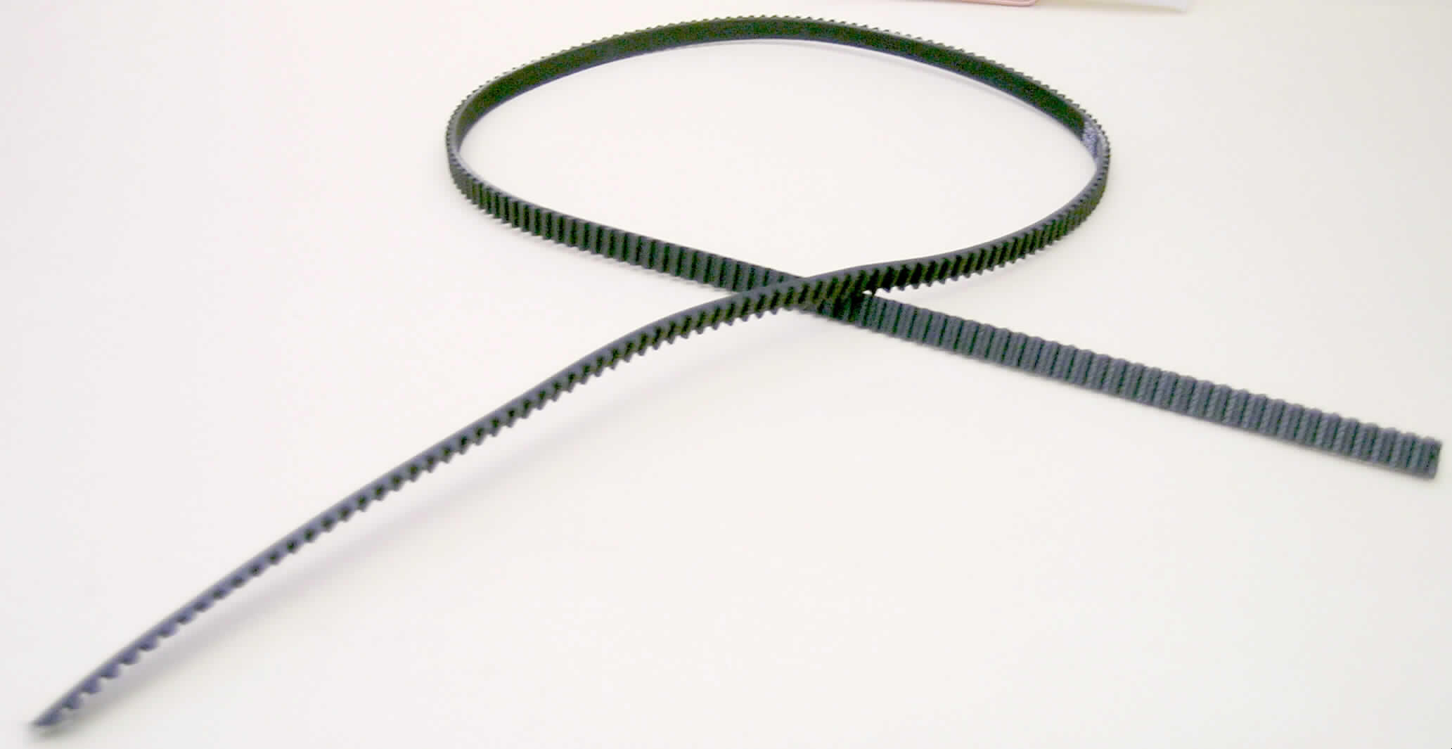 Synchrontreibriemen (Zahnriemen) mit einem äußeren Umfang zwischen 60 und 150 cm

Ein vorgelegtes Warenmuster hatte folgende Eigenschaften:
Schwarzer Synchrontreibriemen mit einem Umfang von ca. 80 cm und einer Breite von ca. 0,6 cm. Der Treibriemen zeigt auf der Innenseite ein Zahnprofil.

Analytische Ergebnisse:
IR-Spektrum: schwarze Kautschukmasse im Wesentlichen wie Kautschuk
Schwefelnachweis: positiv                      
Burchfieldtest: Hinweis auf Kautschuk
Lupenbild: Kautschuk verstärkt mit Spinnstoffeinlagerungen

Nach den Untersuchungen liegt ein Zahnriemen aus Kautschuk vor, der verstärkt wird durch Spinnstofffasern.