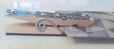 Træklemme holdt sammen med et stykke bøjet metal. På den ene side af klemmen er fastsat et stykke magnet af gummi blandet med pulveriseret jern, agglomeret ferrit. Den anden side er dekoreret med mønster.

Klemmen er ca. 1x7 cm