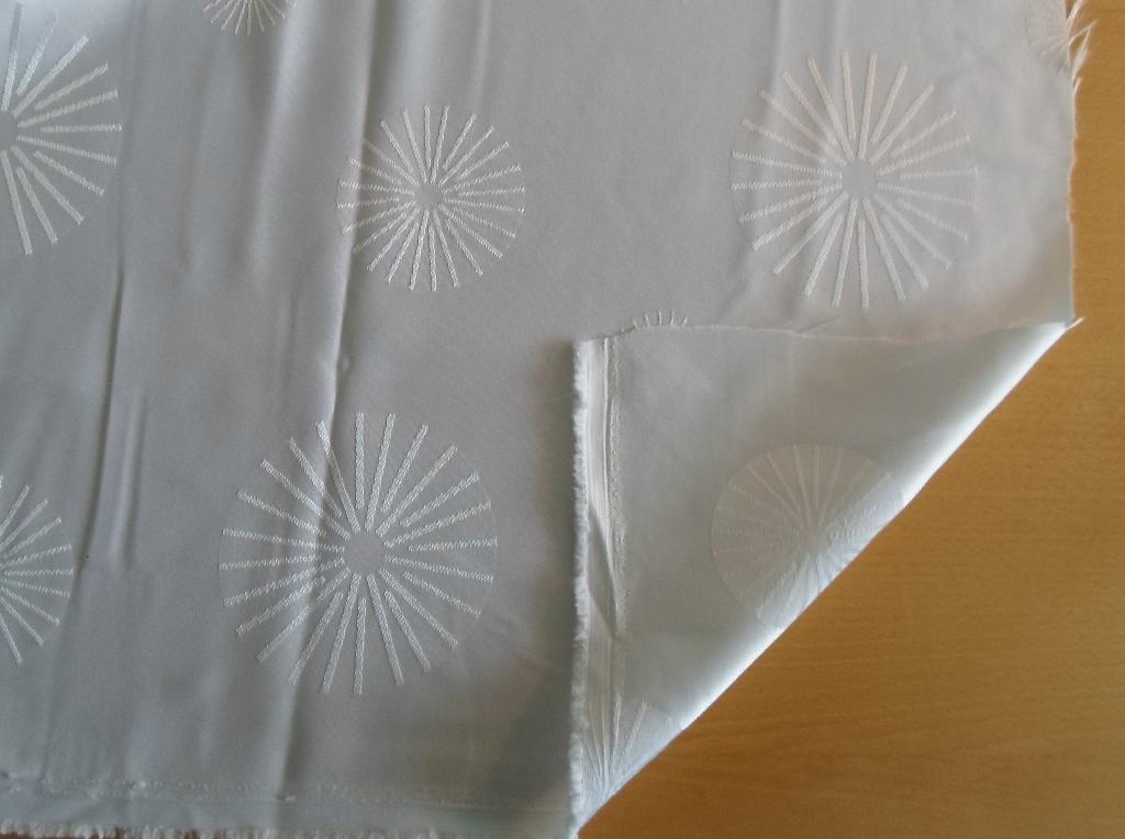 Varen er ifølge det oplyste en vævet metervare, der er fremstillet af 100 % polyester. 

Der er modtaget vareprøve. Vægten er oplyst at være 142 g/m2. Den foreligger i en størrelse på 140 cm x 500 cm og med vævet kant (Loom edge). 

Ifølge den fremsendte vareprøve er vævetypen som vævet stof.

Trådene i stoffet har en hvid farve.  I stoffet er vævet et diskret rundt mønster (jacquard vævet).

Det er forudsat, at varen ikke er kantet.