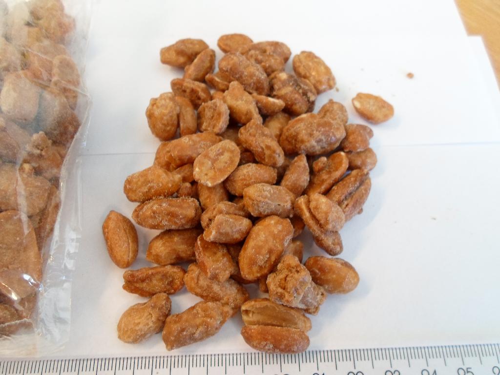 Varen foreligger som en hele peanuts, uden skal, der er helt overtrukket med en tyk skal af karamelliseret sukker. Den tykke skal af kanaliseret sukker varierer i tykkelse.
Varen er en fødevare.
Følgende er oplyst:
Peanuts		xx,00 % 
Sukker		xx,00 %
Glukose		 x,00 %
Solsikkeolie    x,00 %
Arabisk gummi	< x,00 %
Solsikke lecithin< x,00 %
Honning		< x,00 %
Ved gennemskæringen af varen ses det, at varen er brunlig og det er svært at se hvor grænsen mellem sukker lag og peanut er. Skallen af sukker omkring peanutsene er hård.

Varen smager meget sødt af sukker og lidt af peanut.

Varen forlægger som bulk vare og i pakker til detailsalg.