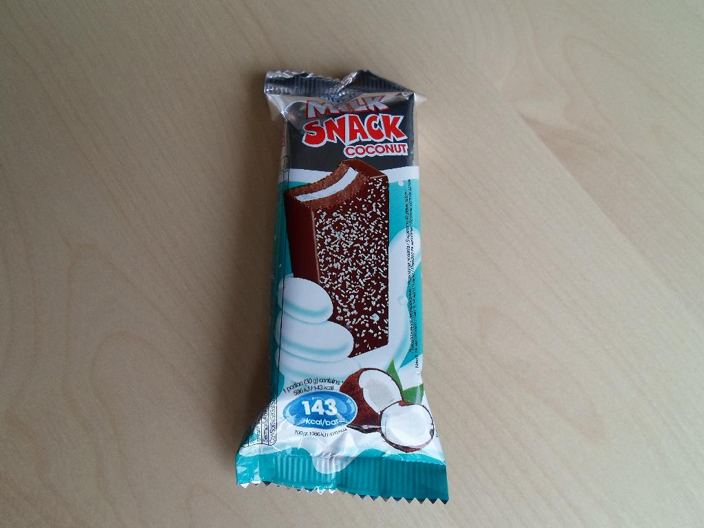 Varen kaldet ”Milk Snack Coconut” af mærke Milino foreligger som en mørkebrun bar, der er fuld overtrukket med mørk chocolade. Den dufter af kokos og er dækket med lidt revet kokos på oversiden.

Baren måler ca. 8,8 x 3,7 x 1,8 cm, og den består af to lag tynde plader af brun kage og i midten er der en hvid creme. 

Detailsalgsemballagen er en metaliseret plastfolie med sølv og grøn-blå baggrundsfarver.

Efter angivelsen på emballagen er nettovægten 30 g.

Varen er en mælkesnitte bestående af to lag kage, og kan betegnes som slik.

Ifølge de medsendte dokumentationer kaldet ”Product and Logistic Data” og ”Product data sheet”, er angivelserne over ingredienser og sammensætning ikke ens i de to dokumenter. 

Ifølge ”Product and Logistic Data” indeholder varen følgende ingredienser: 25 % sukker, 25 % vegetabilsk fedt (palmolie, palmekerneolie, kokosolie), 18 % sødmælk, 10 % hvedemel, 5 % fedtfattigt kakao, 4 % glucose-fructose sirup, 2 % mælkeproteiner, æggepulver, sødmælkspulver, kartoffelstivelse, valllepulver, aromastoffer, lactose, emulgatorer, vand og bagepulver. Der er desuden angivet at varen består af 33 % kage, 30 % icing og 37 % creme.

Næringstabellen på medsendt dokumentation angiver følgende: 28 % fedt, 53 % kulhydrater, herarf 36 % sukker og 5,3 % protein. 

Ifølge angivelsen indeholder både kagepladerne og fedtglasuren kakao.

Varen er blød og kagepladerne er luftige som kage plejer at se ud, den smager sødt af kokos og chokolade, og lidt af mælk.