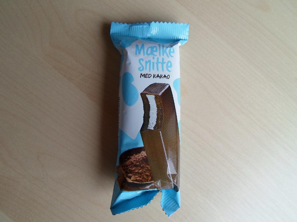 Varen kaldet ”Mælkesnitte med kakao” foreligger som en mørkebrun bar, der er fuld overtrukket med mørk chokolade. Varen er indpakket i en metalbelagt plastfolie med lyseblå og hvid baggrund.

Baren måler ca. 8,8 x 3,7 x 1,8 cm, og den består af to lag tynde plader af brun kage og i midten er der en hvid creme.

Efter angivelsen på emballagen er nettovægten 30 g.

Varen er en mælkesnitte bestående af to lag kage, og kan betegnes som slik.

Ifølge medsendt dokumentation kaldet ”Product- and Logistic Data” og ingredienslisten på varens emballage indeholder varen følgende: 26 % sukker, 25 % vegetabilsk fedt (palmeolie, palmekerneolie, kokosolie), 18% sødmælk, 10 % hvedemel, 5 % kakao, 4 % glucose-fructose sirup, 2 % mælkeproteiner, æggepulver, sødmælkspulver, kartoffelstivelse, vallepulver, aromastoffer, lactose, emulgatorer, vand, bagepulver.

Varen indeholder ifølge medsendt dokumentation følgende: 28 % fedt, 53 % kulhydrater, heraf 36 % sukker og 5,3 % protein.

Ifølge angivelsen indeholder både kagepladerne og fedtglasuren kakao.

Varen er blød og kagepladerne er luftig som kage plejer at se ud. Den smager af chokolade og lidt af mælk. Varen dufter af kakao.