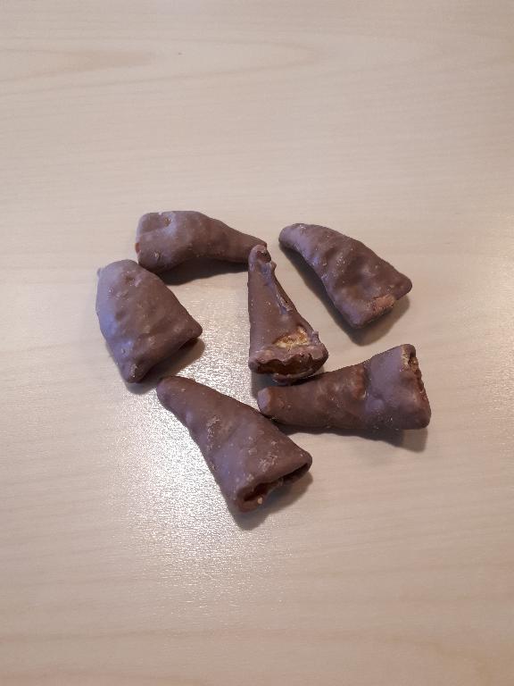 Varen foreligger som flade, ujævn formede kræmmerhuse. Kræmmerhusene er næ-sten fuldt overtrukket med mælkechokolade chokolade.
Varen er en fødevare/ snack.
Ingredienslisten angiver følgende indhold: sukker, mælkepulver, majsmel, kakao-smør, kakaomasse, solsikkeolie, sheaolie, tapiokastivelse, kokosolie, emulgator, hævemiddel, salt og aroma. 

Desuden angives, at varen indeholder mindst XX% kakaotørstof og mindst XX% mælketørstof. 

Ifølge næringstabellen på emballagen indeholder varen: XX% fedt, XX% kulhydrater, heraf XX% sukker, XX% protein og XX% salt. 

På medsendt produktdatablad angives følgende sammensætning af varen: XX% sukker, XX% mælkepulver, XX% kakaosmør, XX% kakao liquor, XX% sojalecithin, XX% salt, XX% majsmel, XX% tapioka stivelse, XX% natriumbikarbonat, XX% shea olie, XX%, solsikkeolie, XX% kokosolie.
Kræmmerhusene måler ca. 4,4 cm i største længde og 2,4 cm i største bredde, de er forskellige tykkelser. 

Varen smager lidt salt og sødt af chokolade. De enkelte stykker er sprøde og lidt bløde i konsistensen.

Varen foreligger i en gul plastpose med angivet nettovægt 100g
