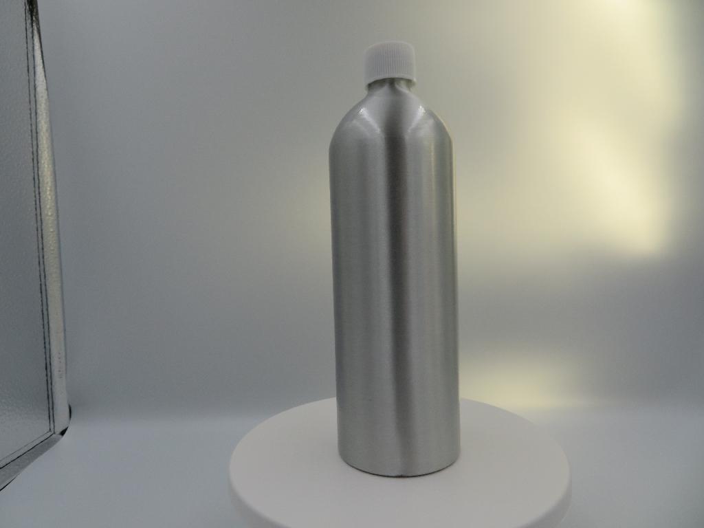 Varen foreligger som en beholder af metal i ét lag. Den har form som en flaske, hvor flaskens hals er bearbejdet med et udvendigt gevind og udstyret med et skruelåg af plast.
Det fremgår af de modtagne oplysninger, at beholderen fyldes med plejeolier til træbordpleje.
Det er oplyst, at beholderen er af aluminium.
Det fremgår af de modtagne oplysninger, at beholderen har en kapacitet på 500 ml og dimensioner på Ø66 x 205mm. 

Beholderen fremstår i en metallisk farve.
Godstykkelsen er oplyst til at være 0,6 mm.